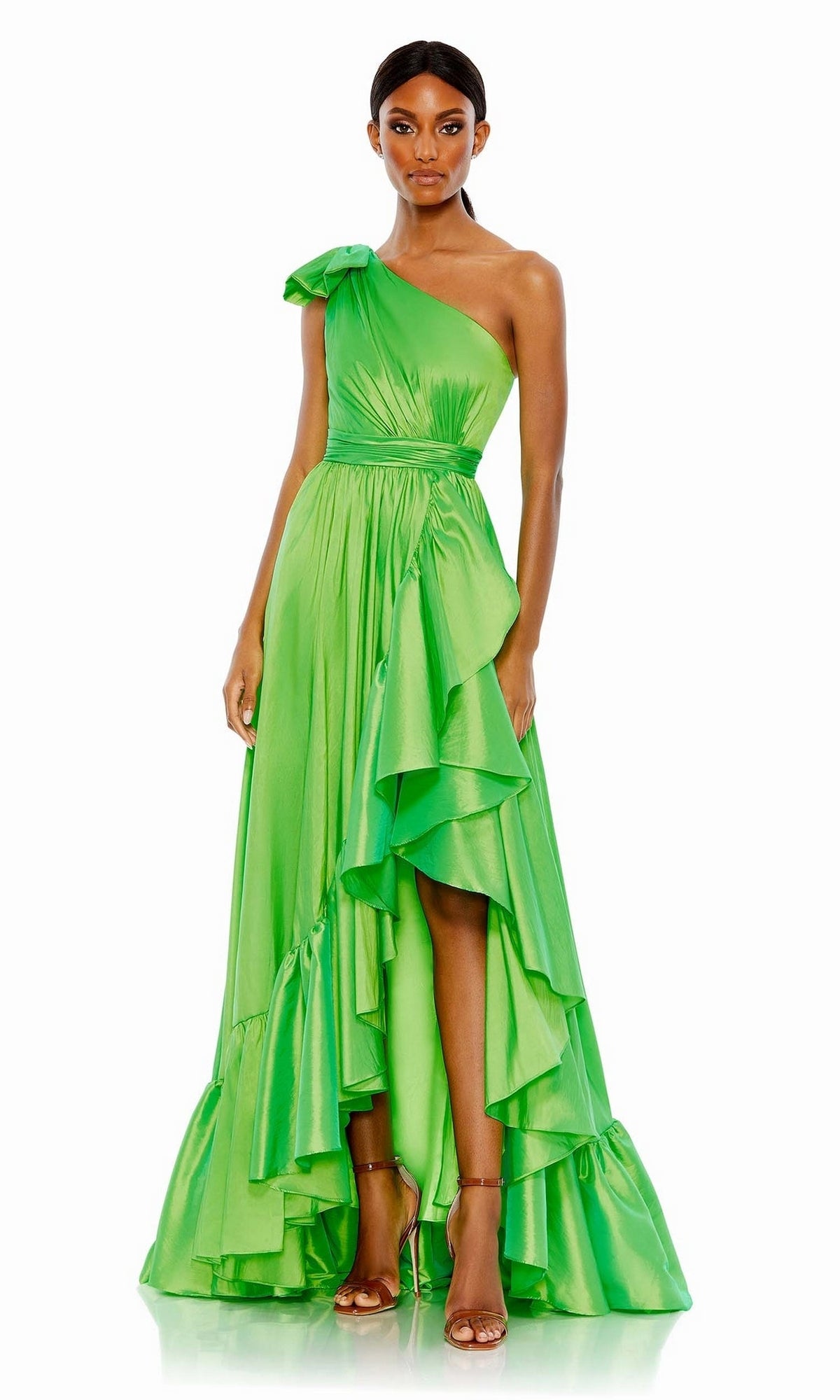 A woman stands against a white background wearing the Long Formal Dress 68027 by Mac Duggal, featuring a bright green hue, one-shoulder design, ruffle tiered layers, asymmetrical hem, and bow detail.